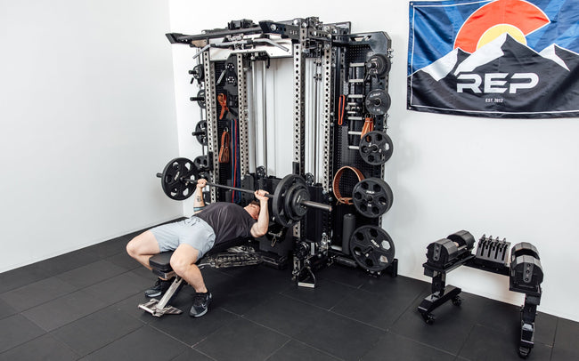 An athlete bench pressing off the front of the Wall-Mounted Ares™ 2.0 while laying on a REP BlackWing™ bench