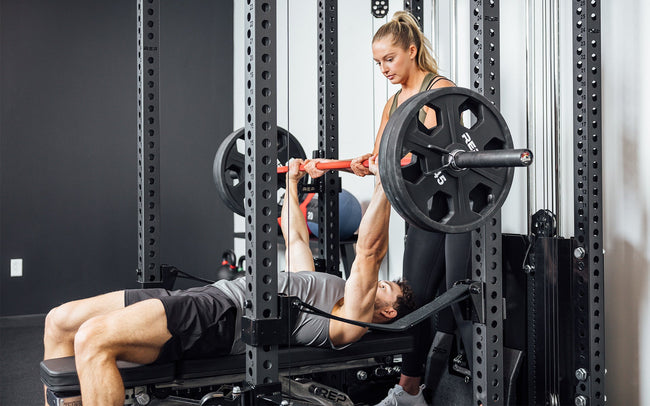 Man doing bench press with a spotter inside a rack that has Ares 2.0